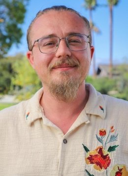headshot of Tim Lewis wearing a ivory collared shirt embroidered with a colorful flower