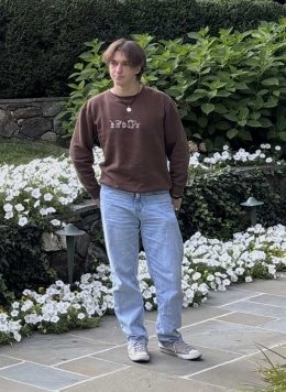Man standing wearing brown sweater and blue jeans.