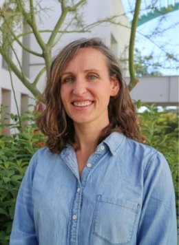 Woman in blue button up shirt with short brown wavy hair.