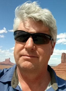 Man in blue shirt wearing black glasses with white short hair.