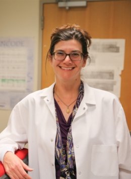 Woman in white science coat with glasses and brown hair.