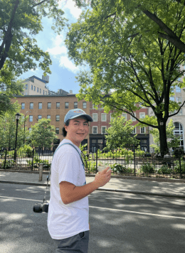 Man wearing white hat and shirt standing in front of trees.