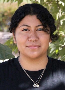 closeup of a student in a black tshirt stands in front of a tree