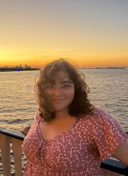 a girl with glasses standing with her back to the sunset over water
