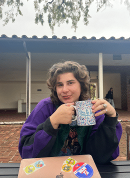 Willow sitting with a mug in their hand in a courtyard