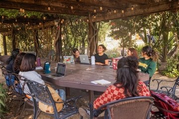 Students sit around a long table with their laptops in the Grove House outdoor classroom.