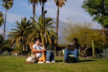 two students sit in chairs ont he mounds with the grove house behind them