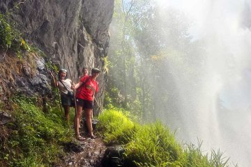 three students hike under a waterfall