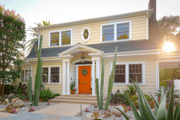 a yellow house with an orange door with the sun setting in the background