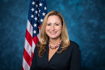 Debbie in front of a blue backdrop and American flag