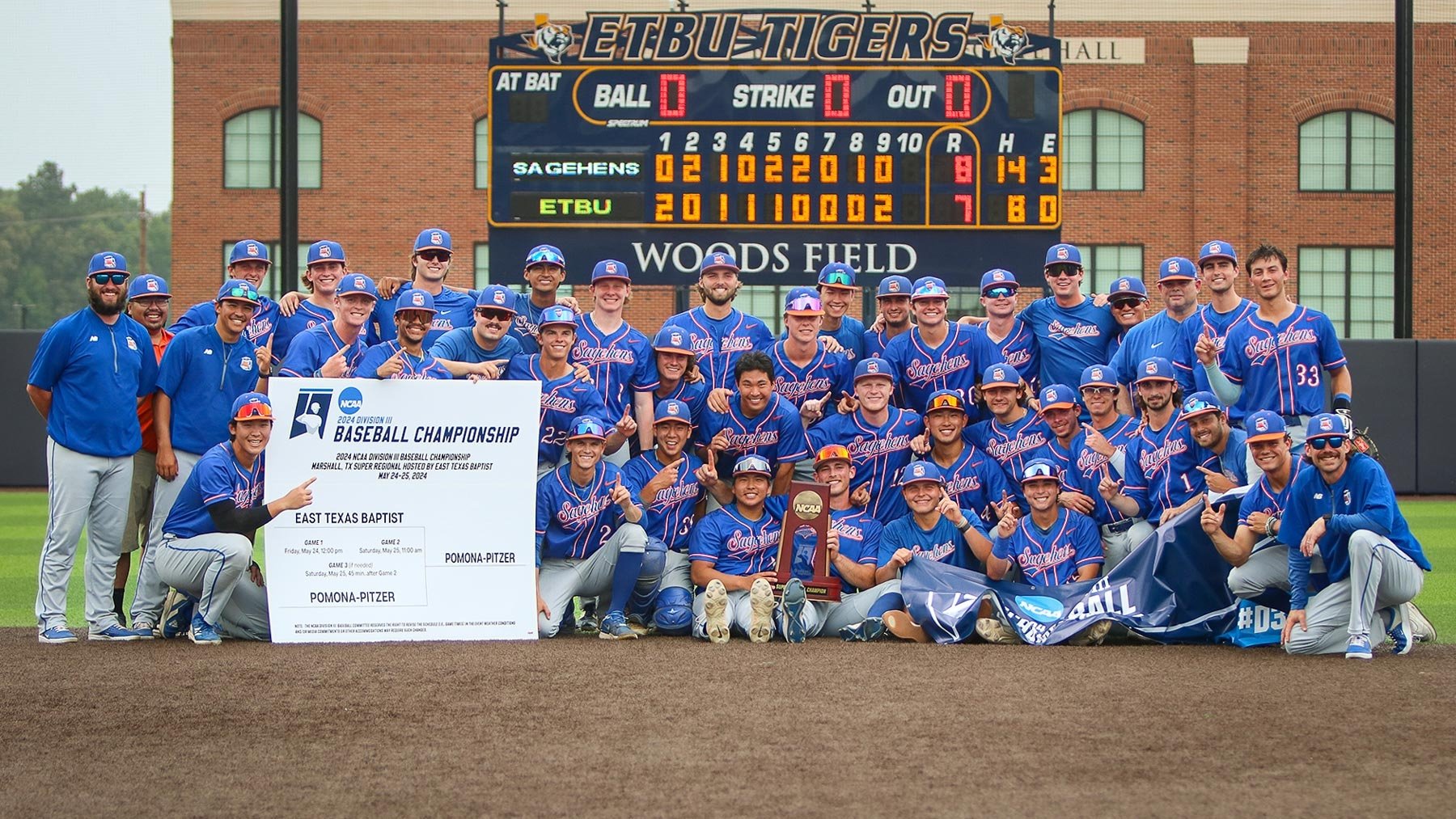 The Pomona-Pitzer men’s baseball team gather on the field in front of the score board with their NCAA trophy.