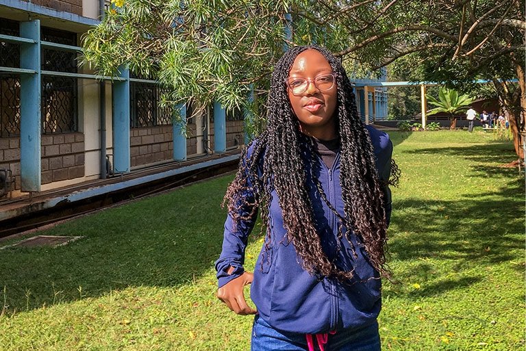 Sia Were wears a navy blue jacket and glasses and has long black hair in braids.
