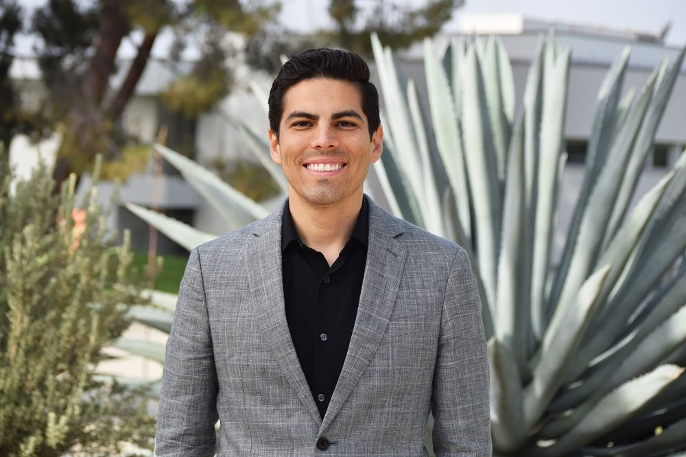 Marcus Rodriguez has short black hair and wears a gray blazer over a black shirt.
