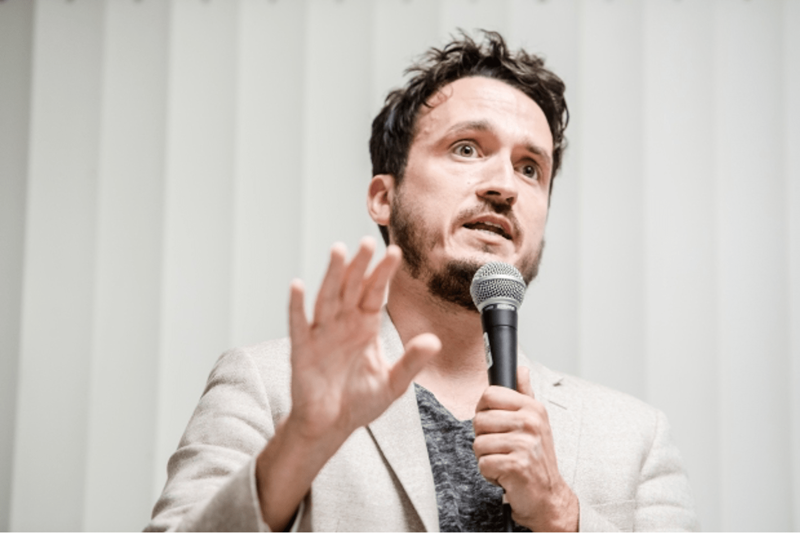 Michael Ceraso speaks on a microphone, wears a white blazer, and has short dark hair and beard.