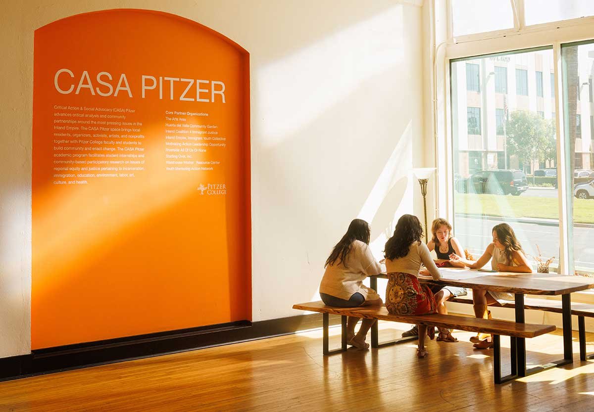 students sit at a table next to the large orange casa pitzer sign