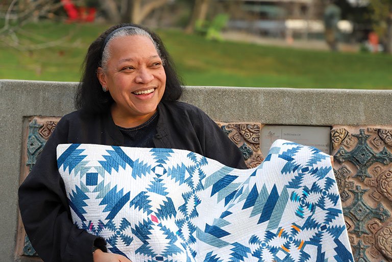 Chawne Kimber sits on a bench on the mounds while holding one of her quilts