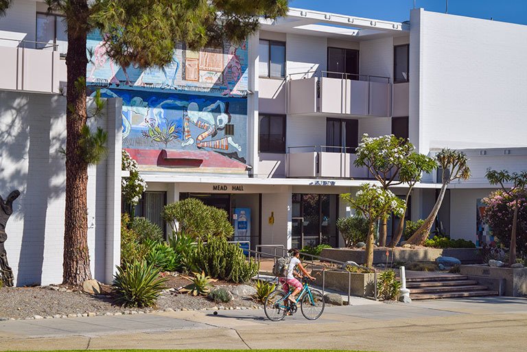 a student rides a bike in front of Mead Hall