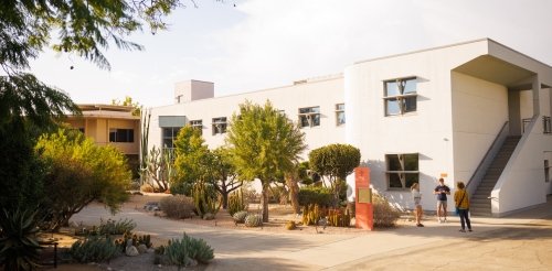 Several students chat outside the large white building of Broad Hall.