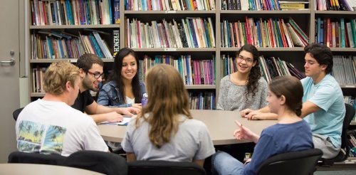 Students gather around a round table in front of a bookshelf.