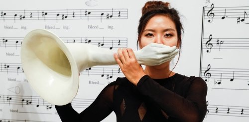 pictures of a woman standing in front of wall of music notes holding a trumpet with a hand as the mouthpiece