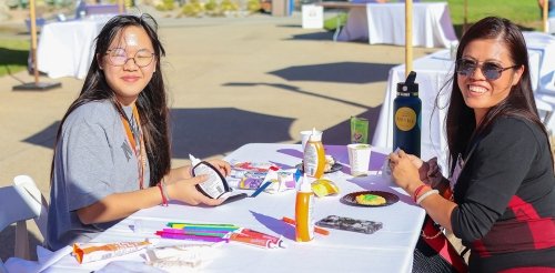 a student and mother sit at a craft table at family weekend