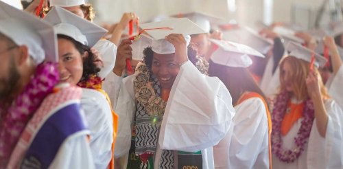 graduates in caps and gowns line up outside the commencement tent