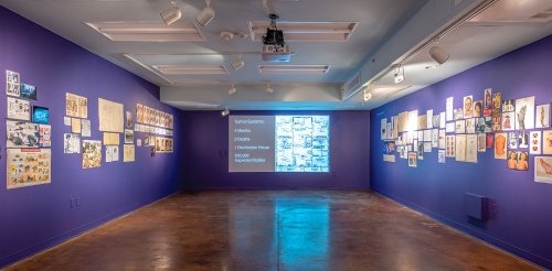 view of an art gallery with blue walls, items hung on the wall, and a screen with an image projected on it