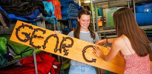 two student work on a Gear Closet sign made out of wood and rope