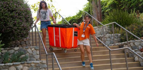 two students carry an orange container down stairs