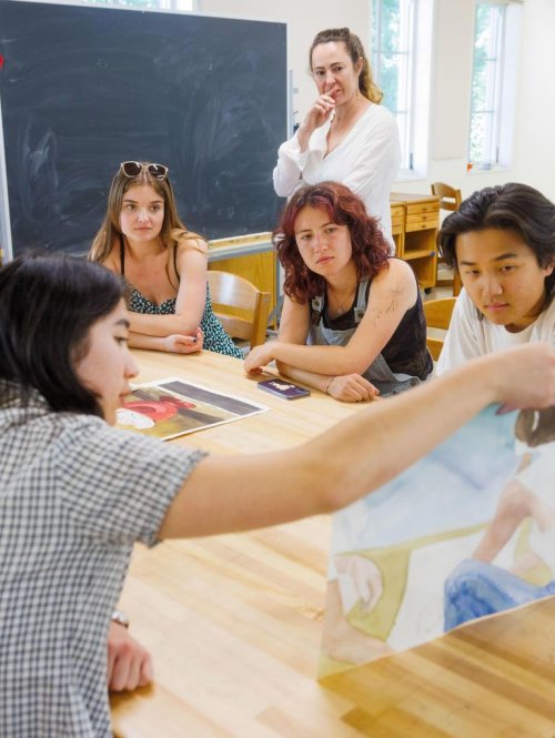 students sit at a table reviewing another's student's artwork
