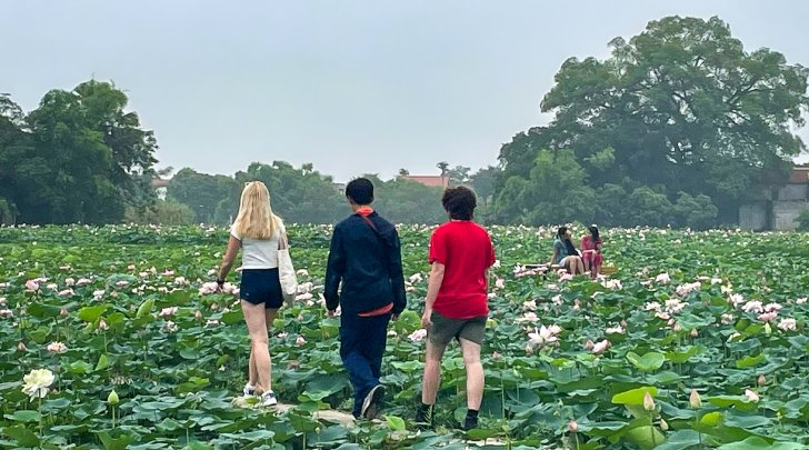 Three students walking through field of lily pads in Vietnam