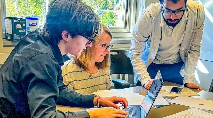 Isabel thacker works with two students at a table in a office