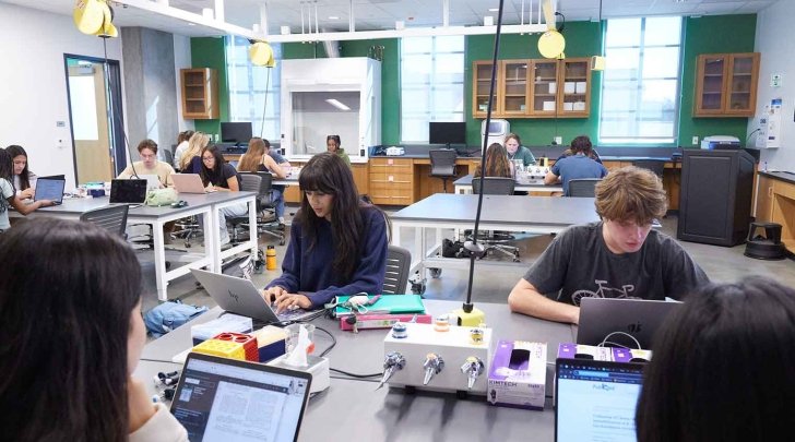 four students sit at a collaborative table in a biology lab
