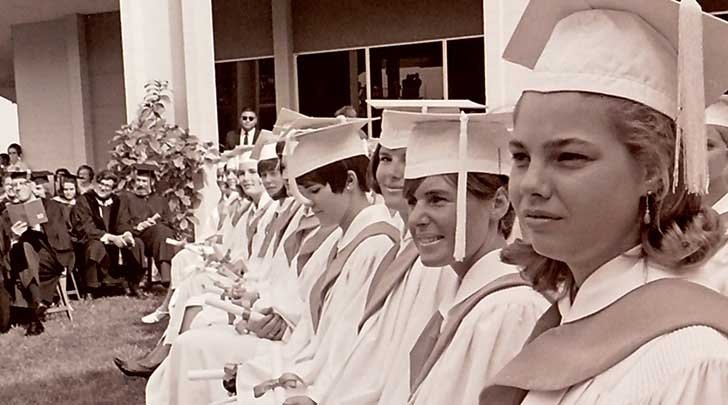 one of pitzer's first graduating classes sits in a row in their graduation attire in the 1960s