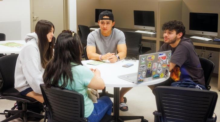 four students sit at a round table in a study room