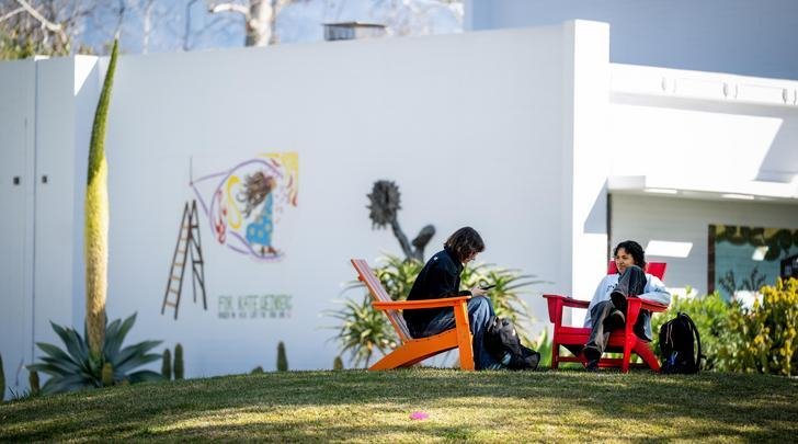 two students sit in adirondack chairs on the mounds in front of mead hall