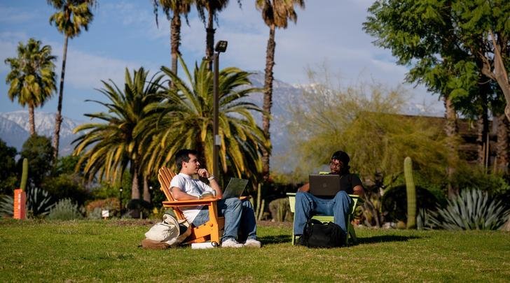 two students sit in chairs ont he mounds with the grove house behind them