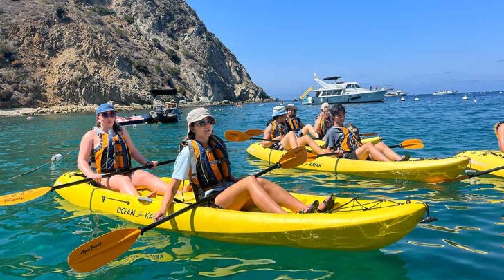 students float in yellow kayaks in the ocean