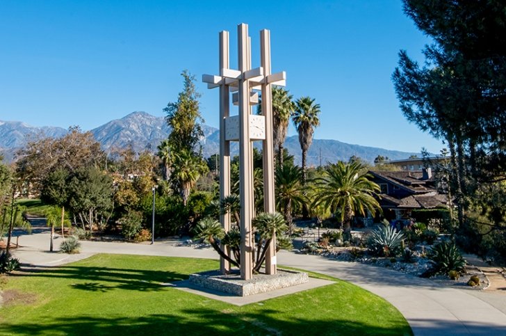 A view of the Pitzer Clock Tower on a bright day with the grove house and the san bernardino mountains behind it. 