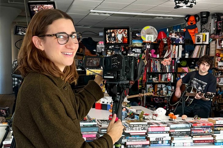 Maia Stern looks over her shoulder and smiles from behind a video camera filming a band playing.