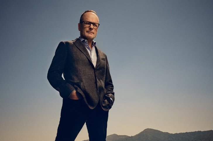John Landgraf wears black-rimmed glasses and a dark suit jacket over a white collared shirt.