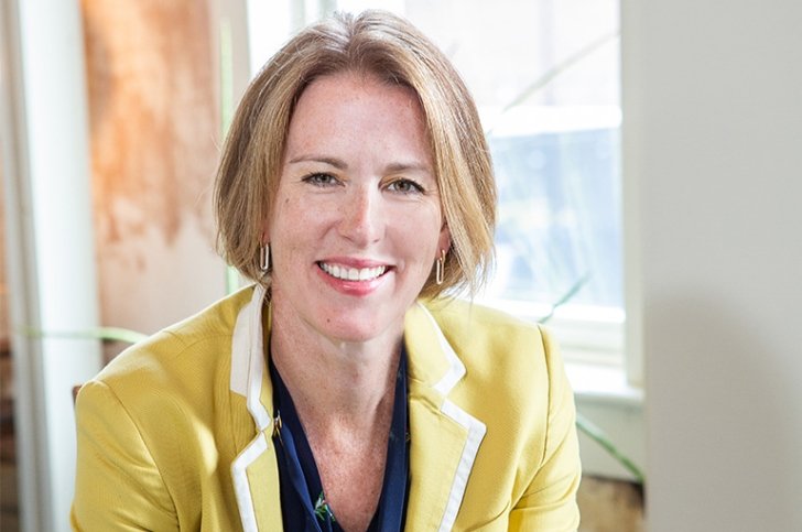 Tricia Milford-Hoyt has straight blond hair in a bob cut and wears a yellow blazer over a blue shirt.