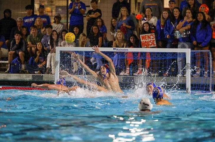 action shot of a mens water polo game with spectators in bleachers in the background