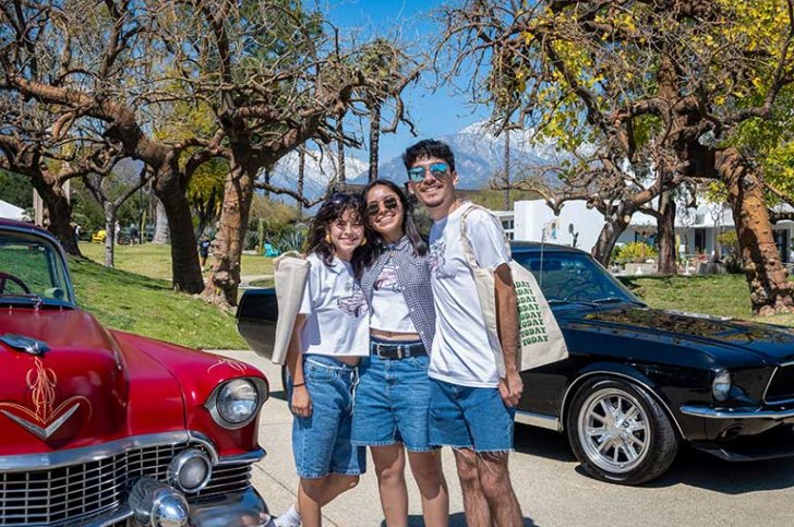 three students pose in front of two classic cars parked near the mounds