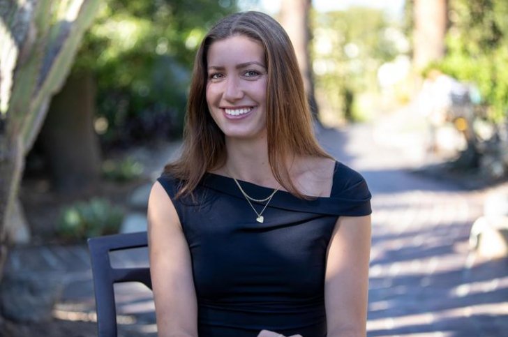 a young woman with brown hair and a black top smiles at the camera