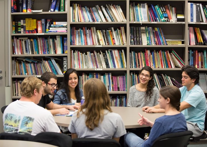 Students gather around a round table in front of a bookshelf.