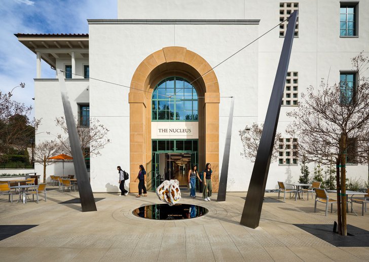 students walk past the arched entrance of the nucleus building on a bright day