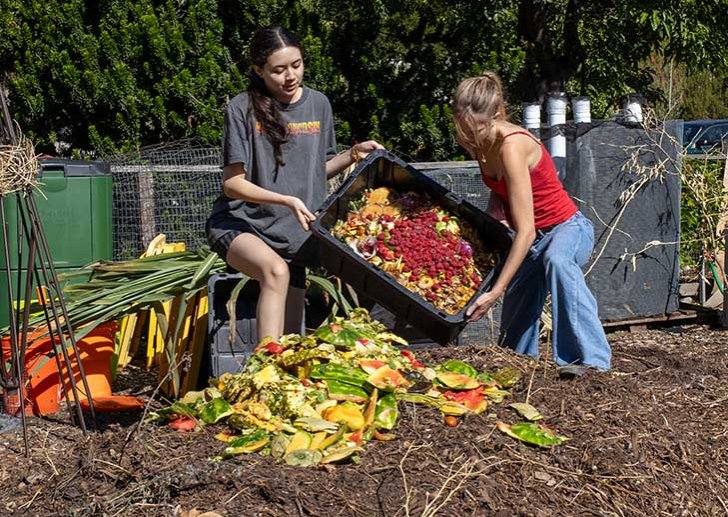 two students dump food scraps onto a compost pile in the pitzer student garden