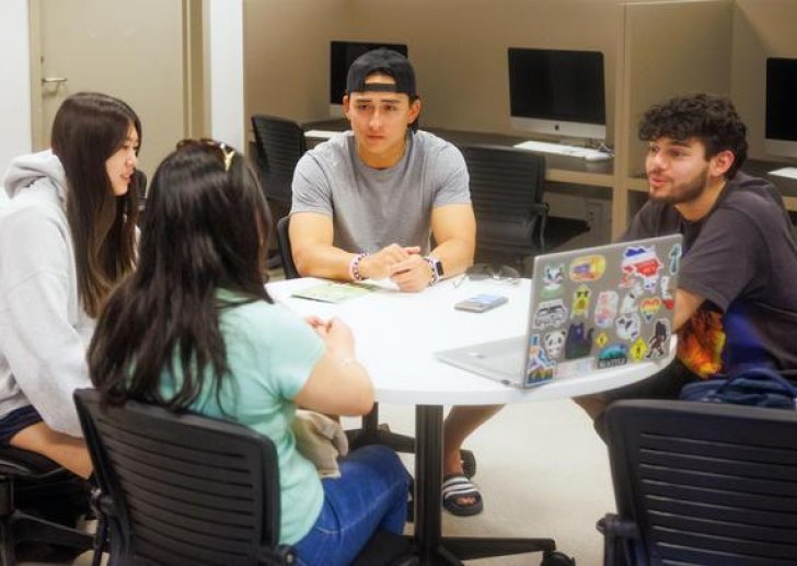 four students sit at a round table in a study room