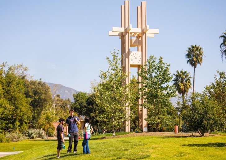three students talk on the mounds with the clock tower in the background